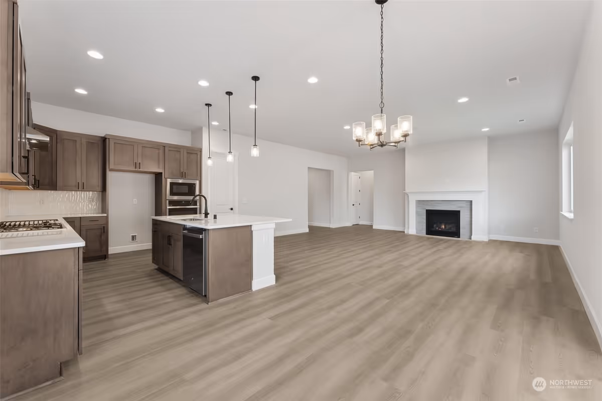 Spacious open-concept living area with kitchen island, dark cabinets, and a fireplace.
