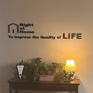 Interior wall with Right at Home logo, plants, and a lamp on a wooden console.
