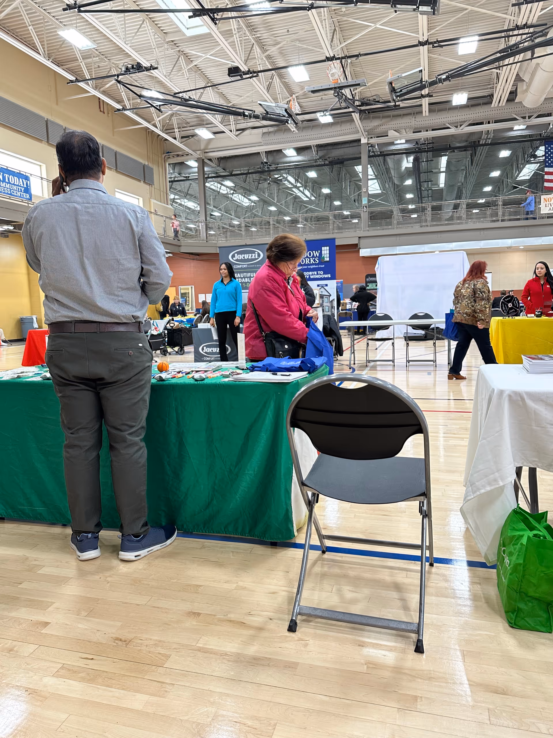 Indoor expo hall with Sahara Home Care booth, tables, and attendees at a community fair.