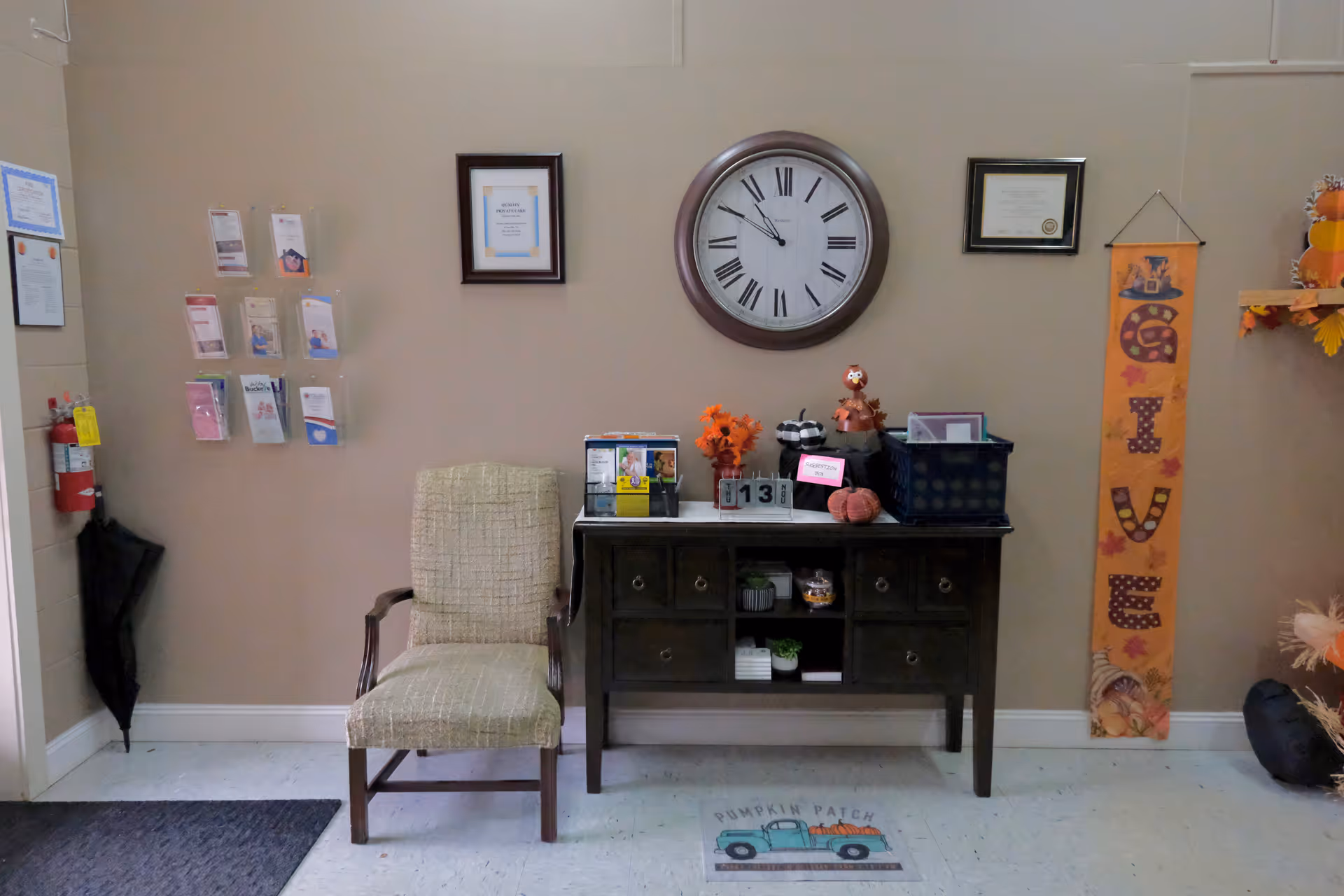 A reception area with a dark console table, clock, chairs, and fall decor.