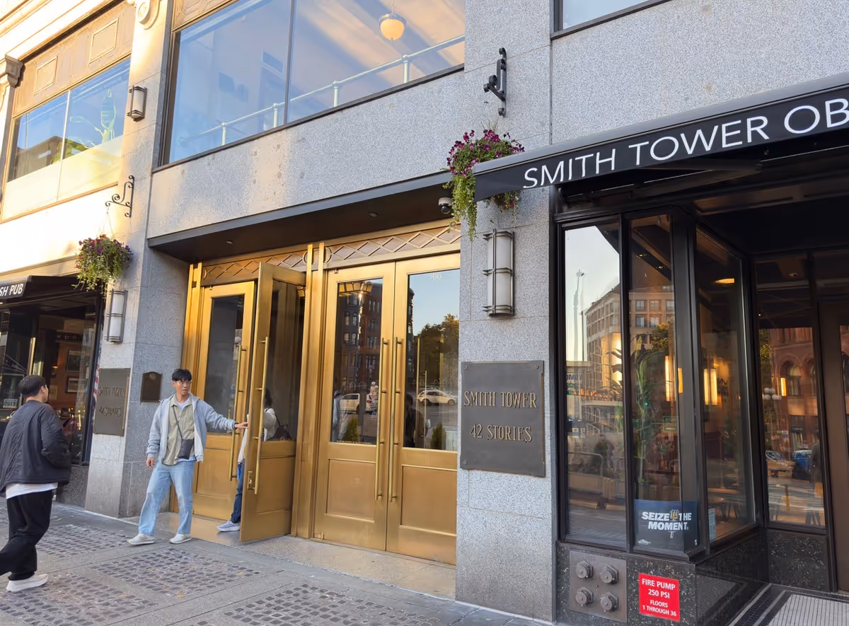 Gold double doors of a modern building entrance with pedestrians on a city sidewalk.