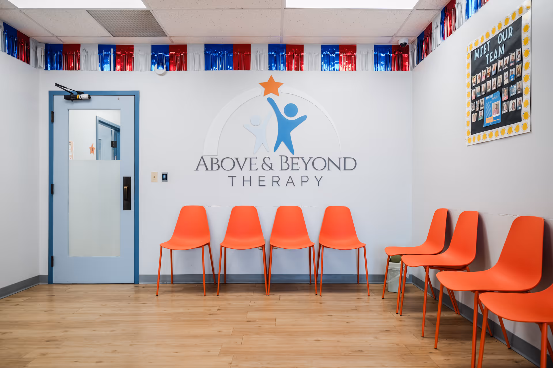 Orange chairs line a white-walled room featuring the Above and Beyond Therapy logo.