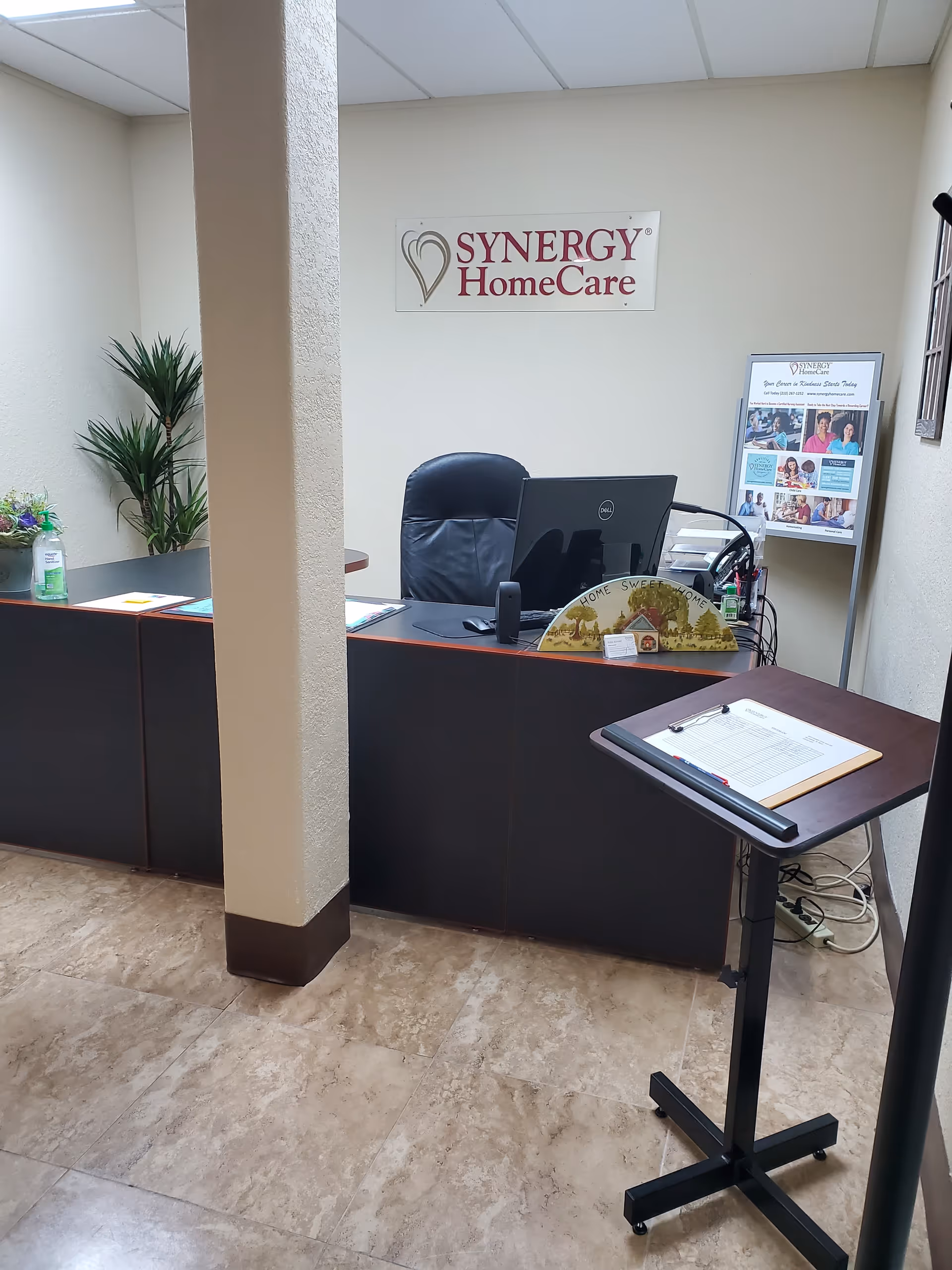 Reception area with a desk, computer, sign, and brochure stand inside a Synergy HomeCare facility.