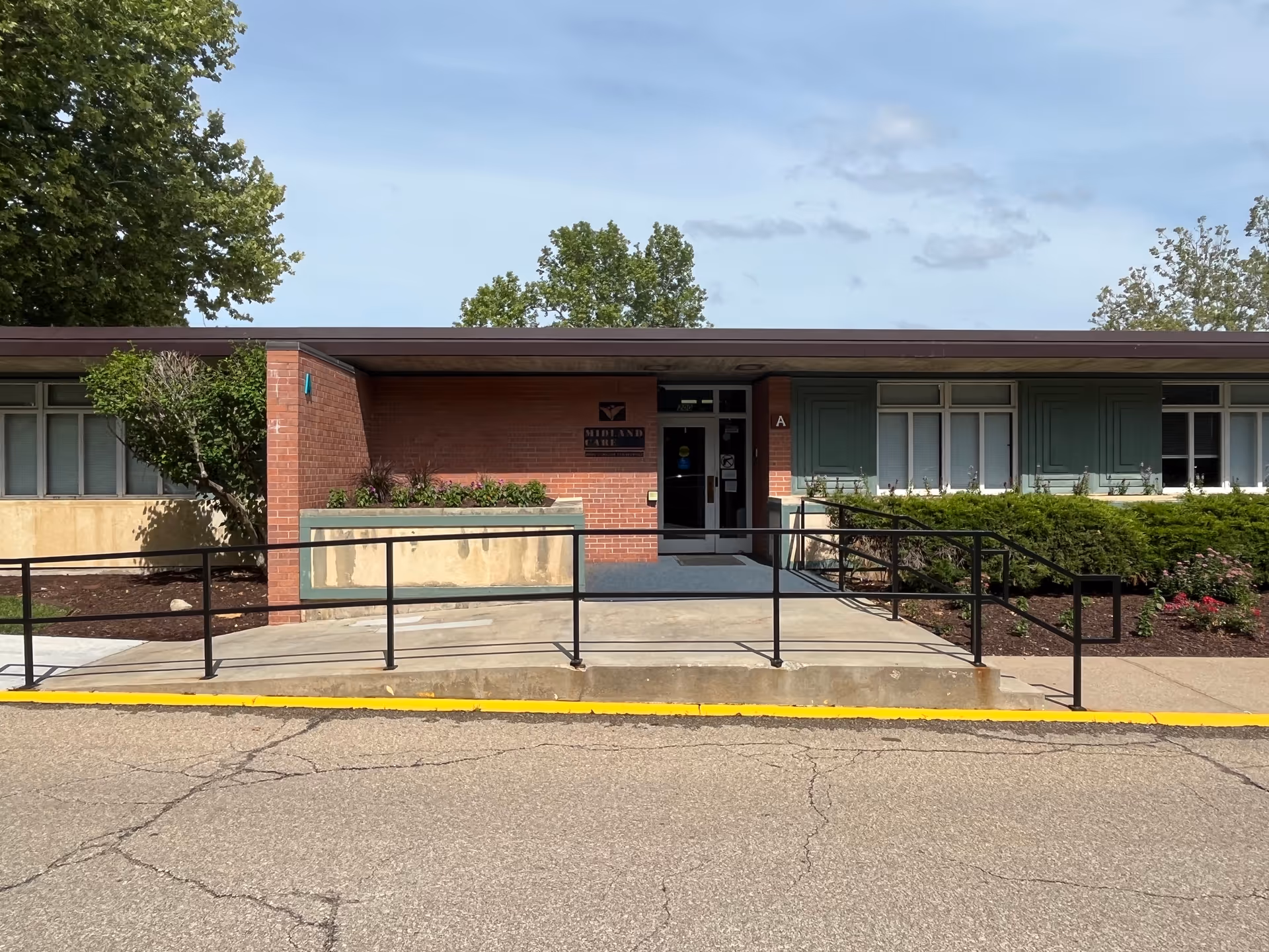 Brick building with a ramped entrance, green shutters, and a sign for Midland Care.