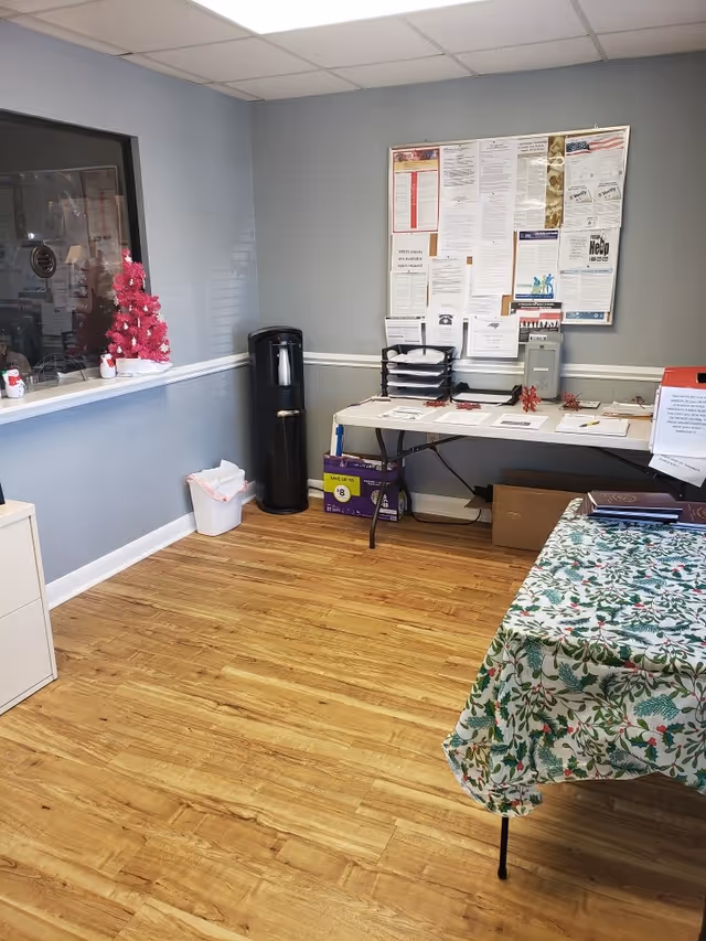 Reception area with bulletin board, papers on a table, water cooler, and floral tablecloth.
