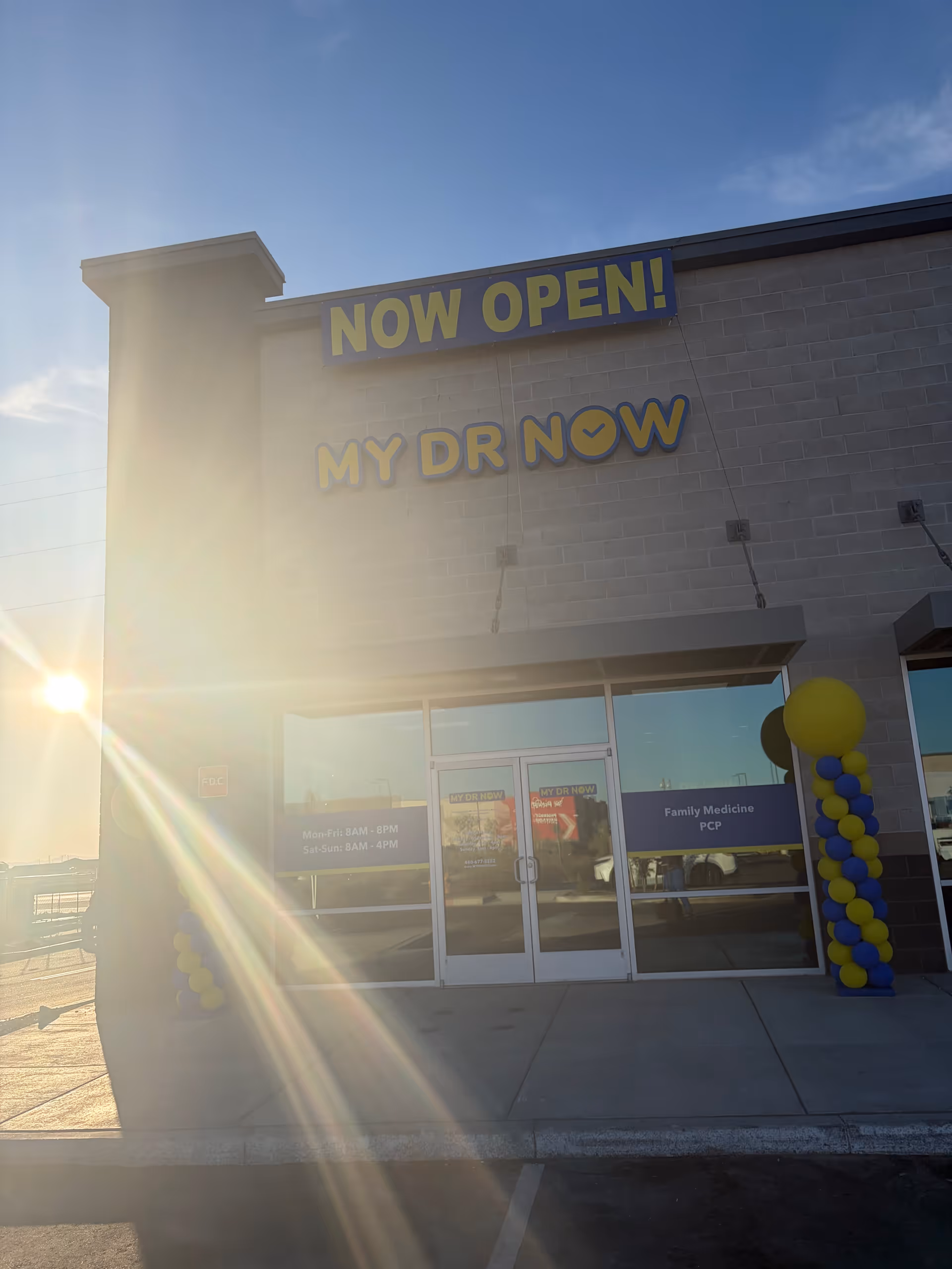 Exterior of a facility with NOW OPEN sign and yellow-blue balloons.