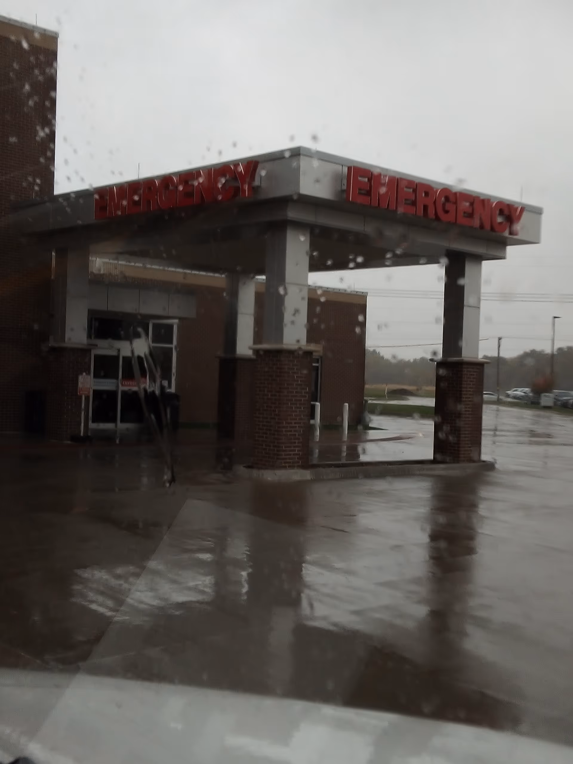 Rainy exterior view of Golden Valley Memorial Healthcare emergency entrance with red EMERGENCY signage.