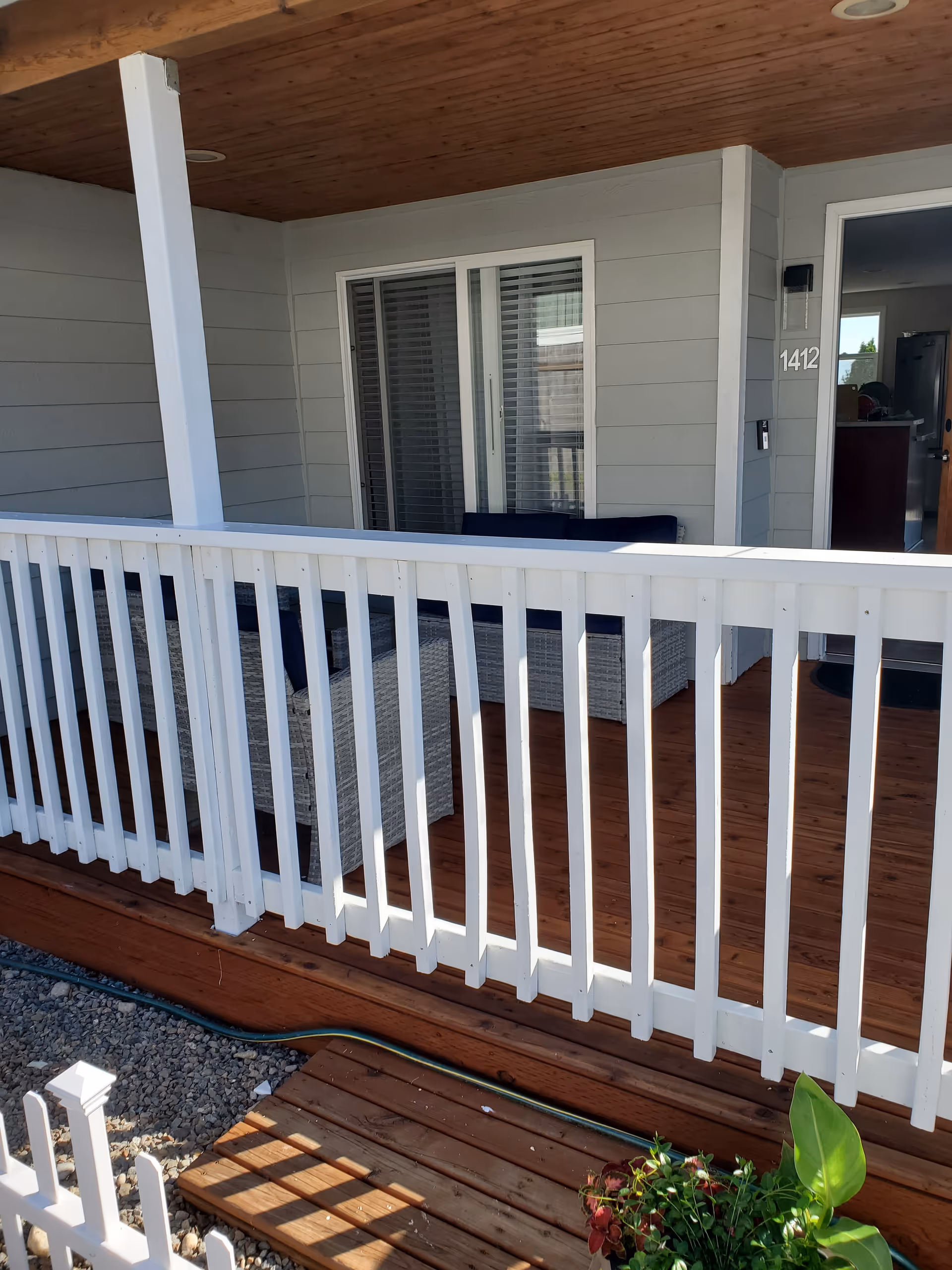 This covered porch features wicker seating and white railing on a wooden deck.
