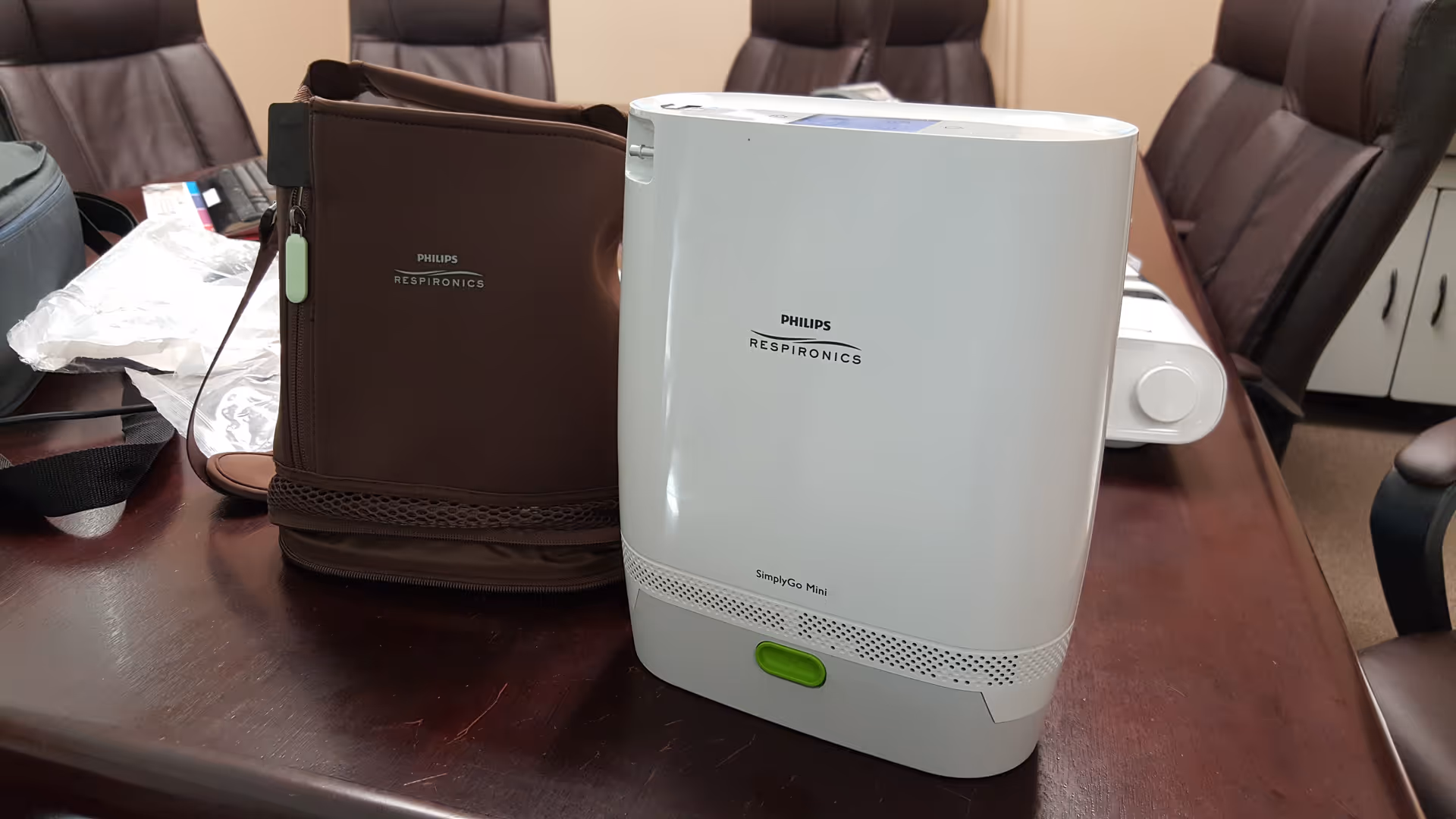 A Philips Respironics SimplyGo Mini oxygen concentrator on a conference table with a brown bag.