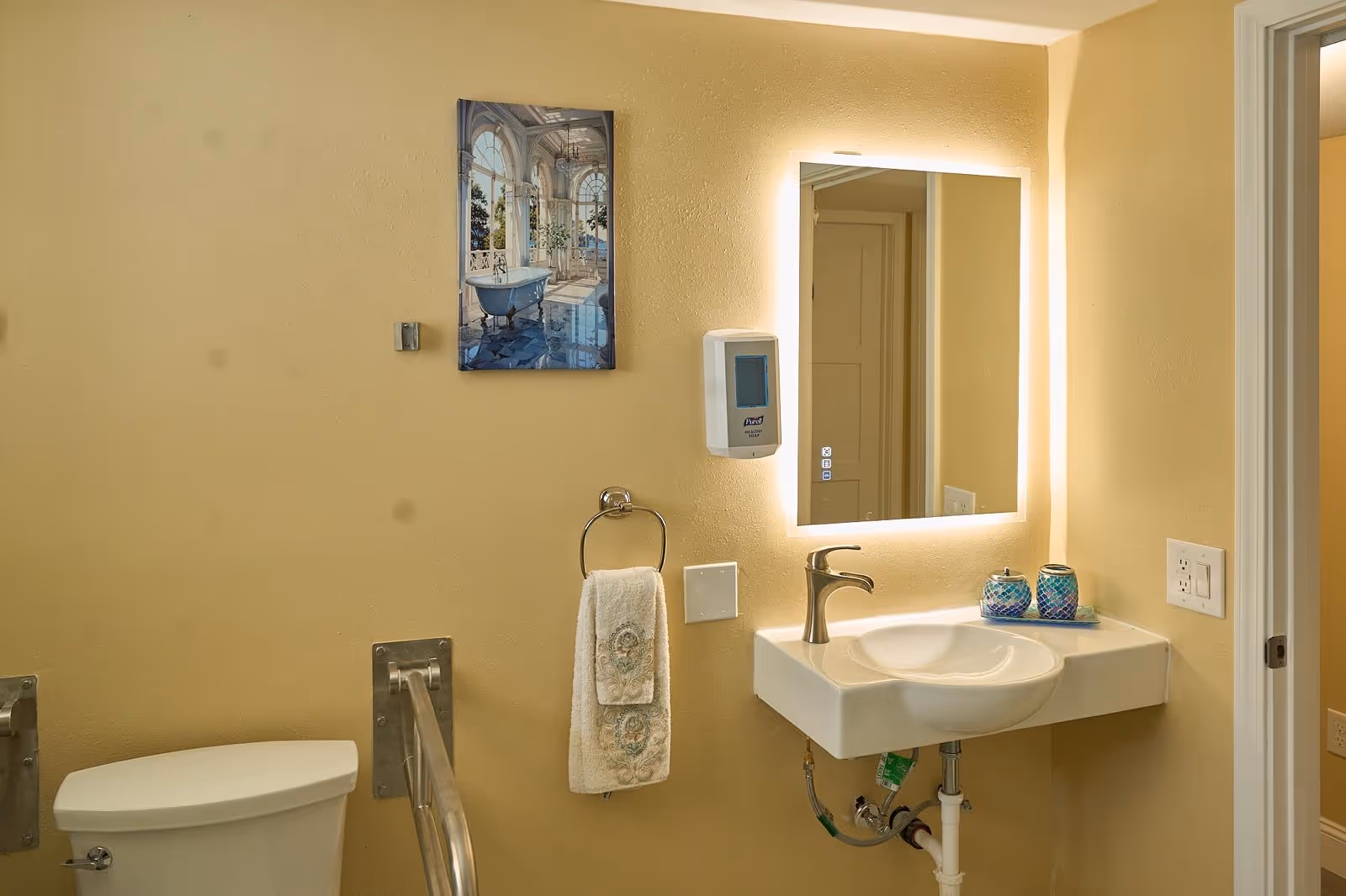 Accessible bathroom with toilet, sink, mirror, towel rack, and wall fixtures.