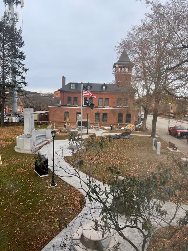 Brick building with flagpoles, a curved walkway, and trees in a park-like outdoor area.