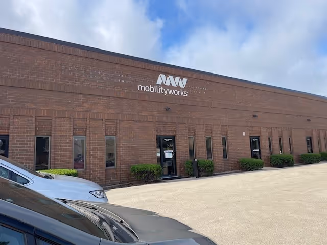 Brick MobilityWorks building exterior with signage, shrubs, and parked cars in front.