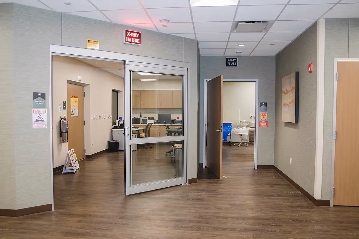 Hospital hallway with glass doors into a treatment area and medical signage.
