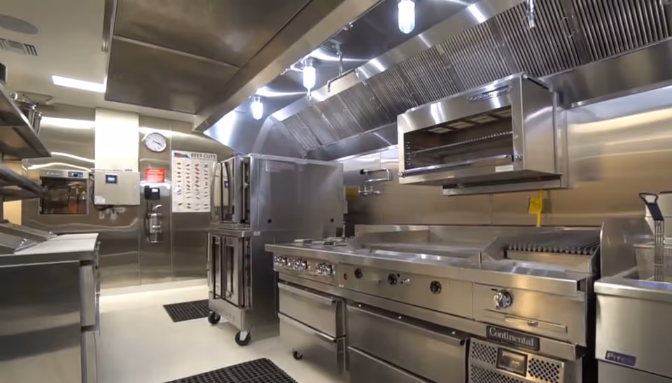 A stainless steel commercial kitchen in Raya's Paradise Inc., with ovens, grills, and overhead vents.
