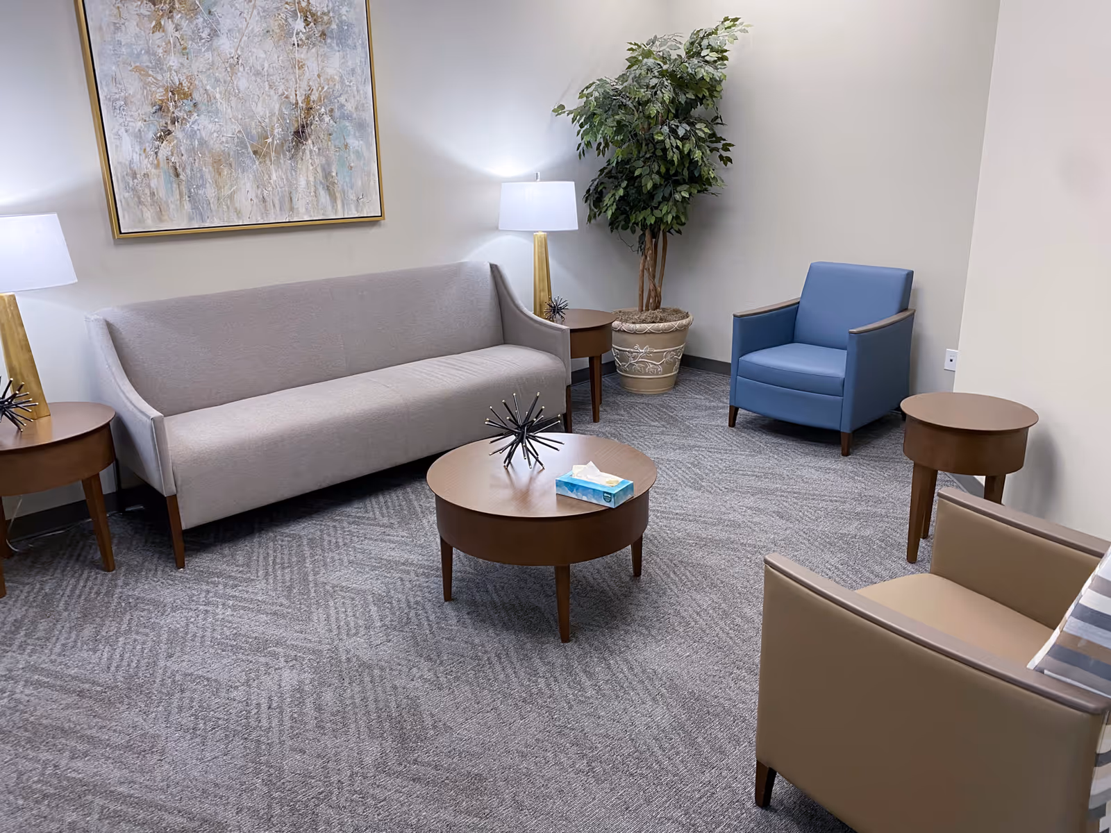 A modern senior living lounge with sofa, blue chair, tables, plants, and artwork.