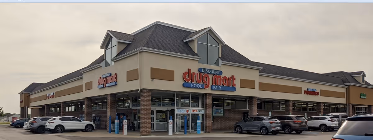 Exterior view of Discount Drug Mart storefront in a strip mall with parked cars.