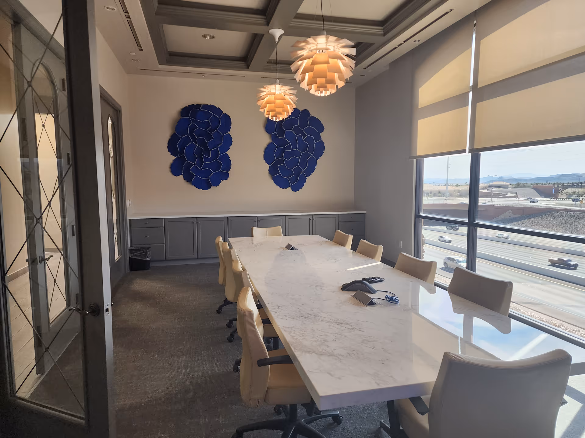Bright interior conference room with marble table, beige chairs, large windows overlooking traffic.