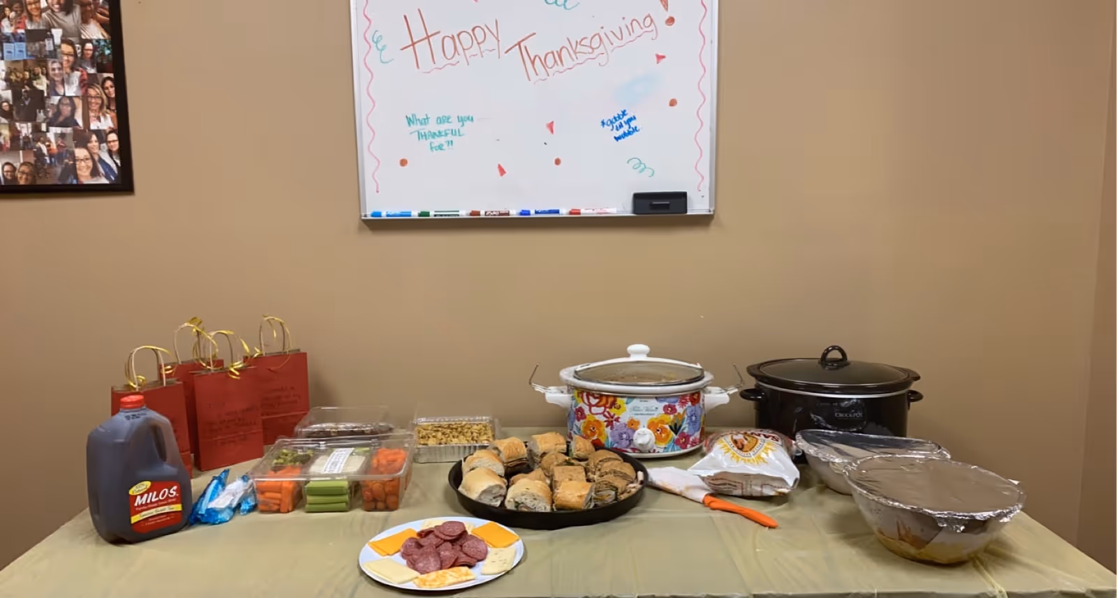 A long table with Thanksgiving foods, crockpots, condiments, and a whiteboard reading Happy Thanksgiving.