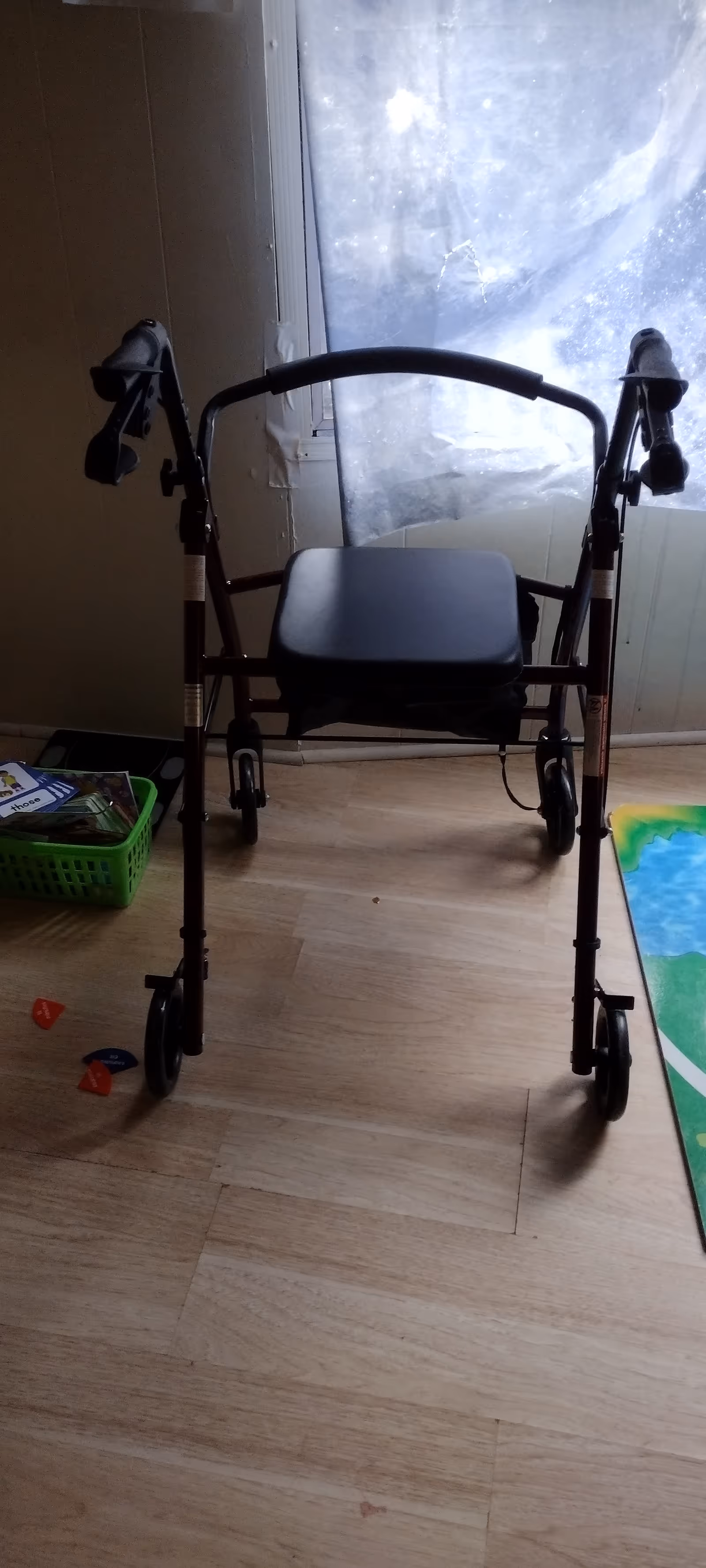 A wheeled walker stands in a sparsely furnished indoor room with a window.