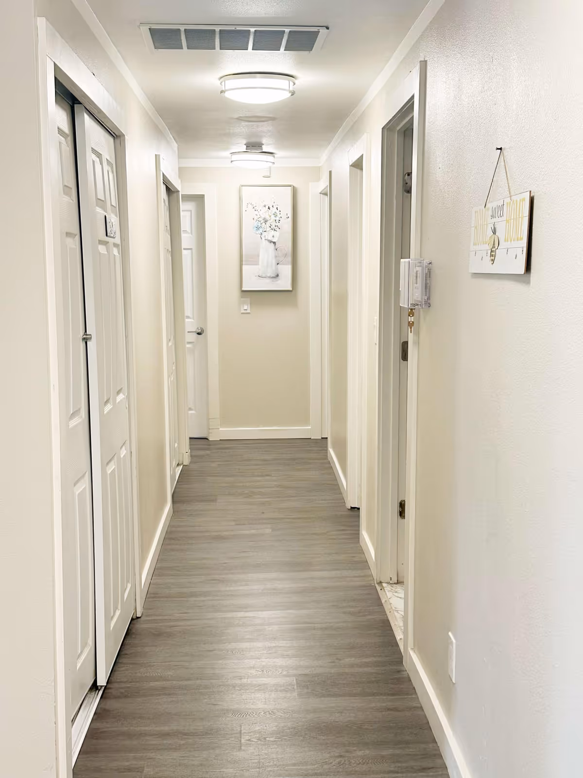 Narrow, well-lit hallway of a senior living facility with multiple doors and artwork.