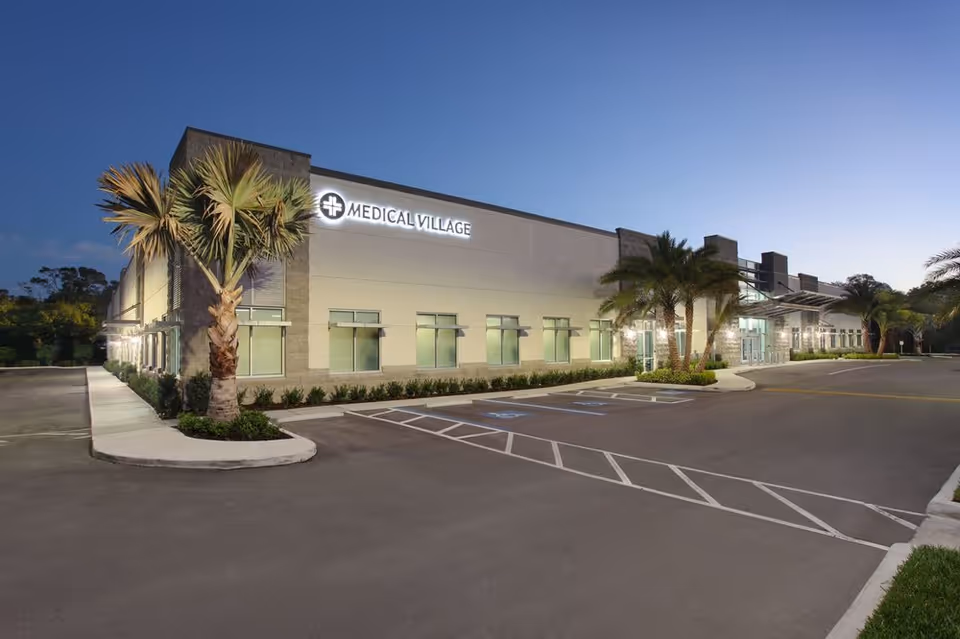 Modern single-story medical building with palm trees, a parking lot, and a clear blue sky.