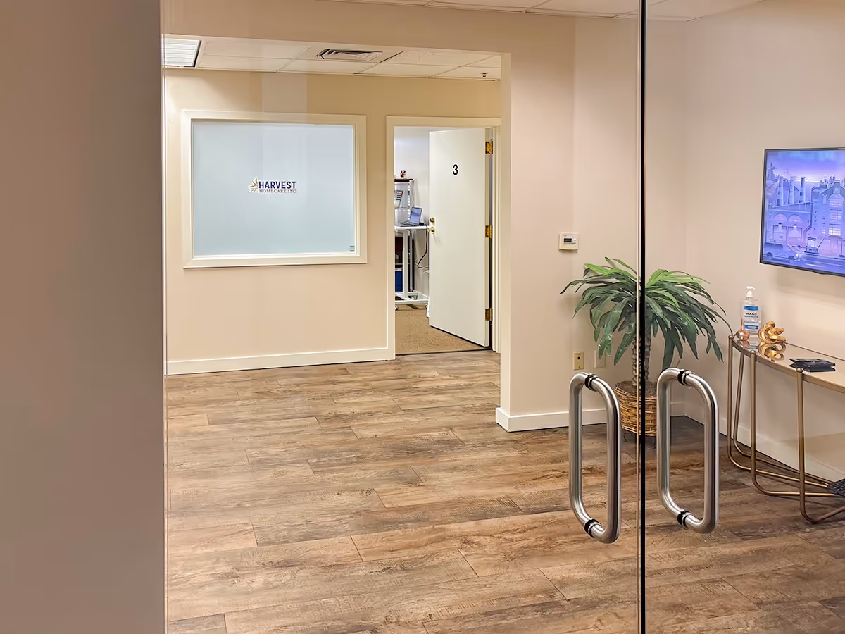 Interior hallway of Harvest Home Care Inc., glass doors, numbered room 3, plant, TV.
