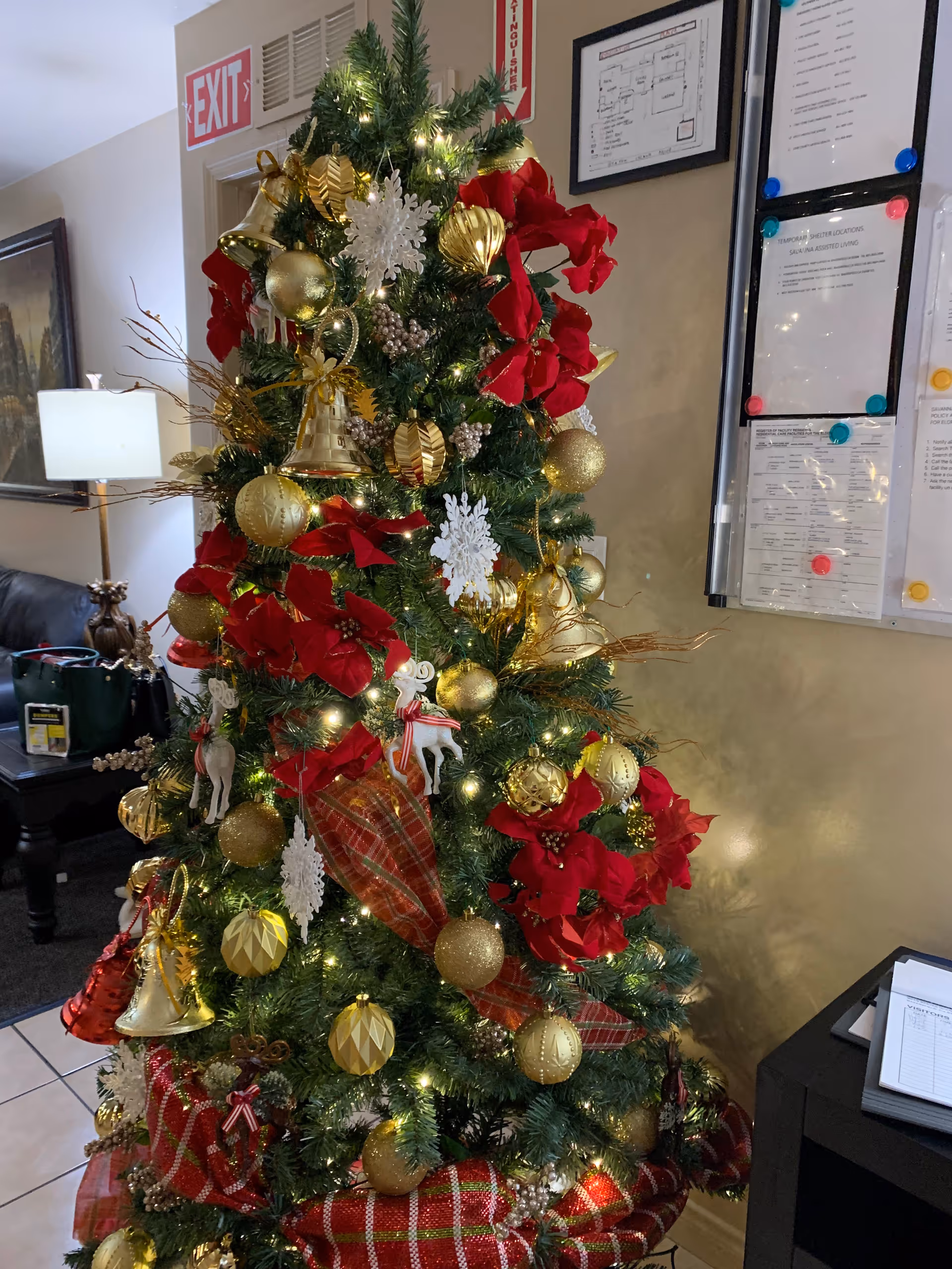 Decorated Christmas tree inside a senior living lobby with red poinsettias and gold ornaments.