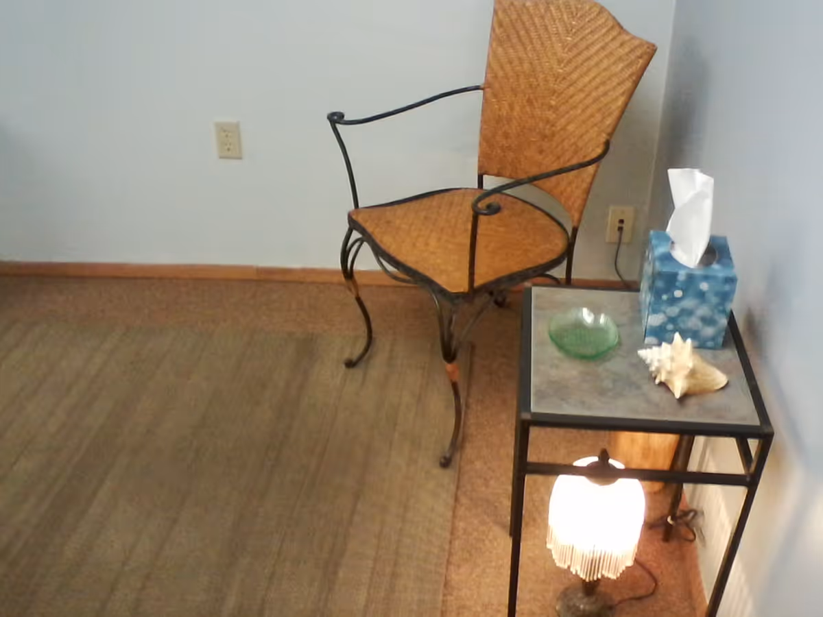 An orange metal-framed chair beside a glass-top side table with tissue box and lamp.