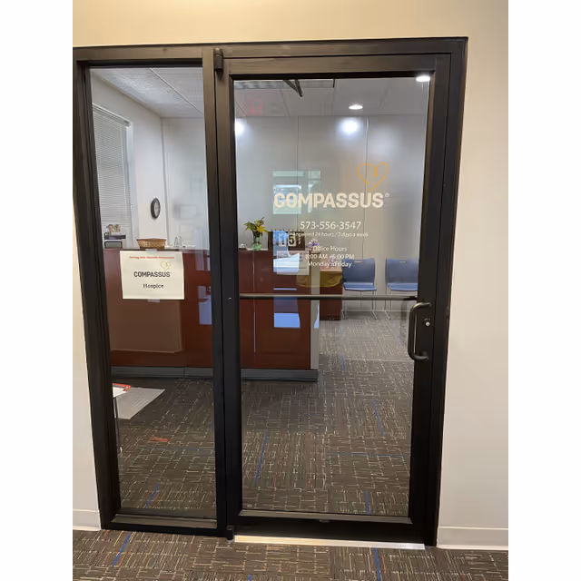 Glass door with Compassus logo leads into a reception area inside a facility.