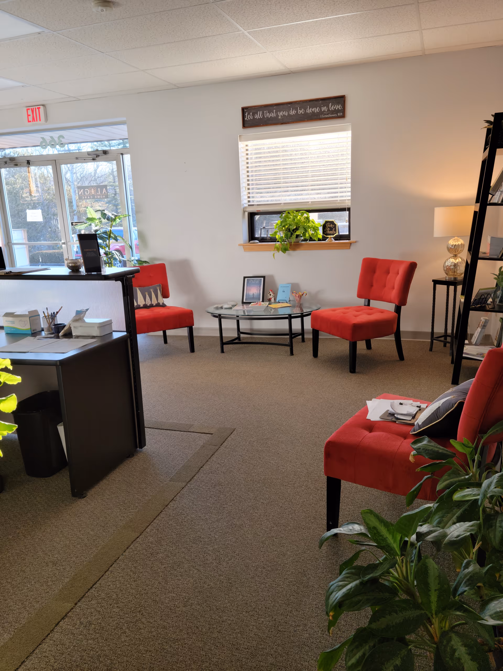 A small welcoming lounge area with red chairs, a glass coffee table, and potted plants.
