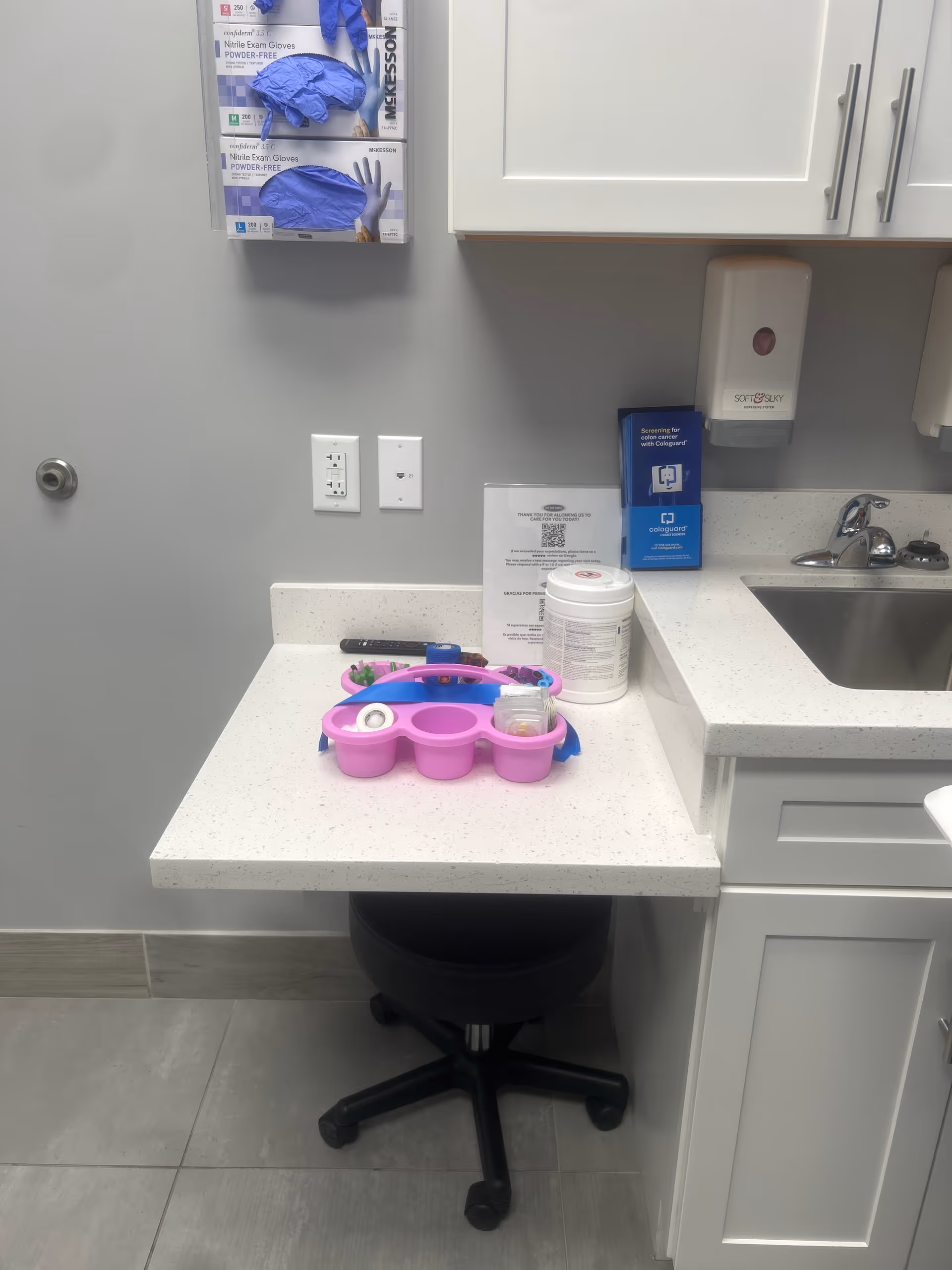 Clinical counter with a pink pill organizer, sanitizer, and a sink in a medical room.
