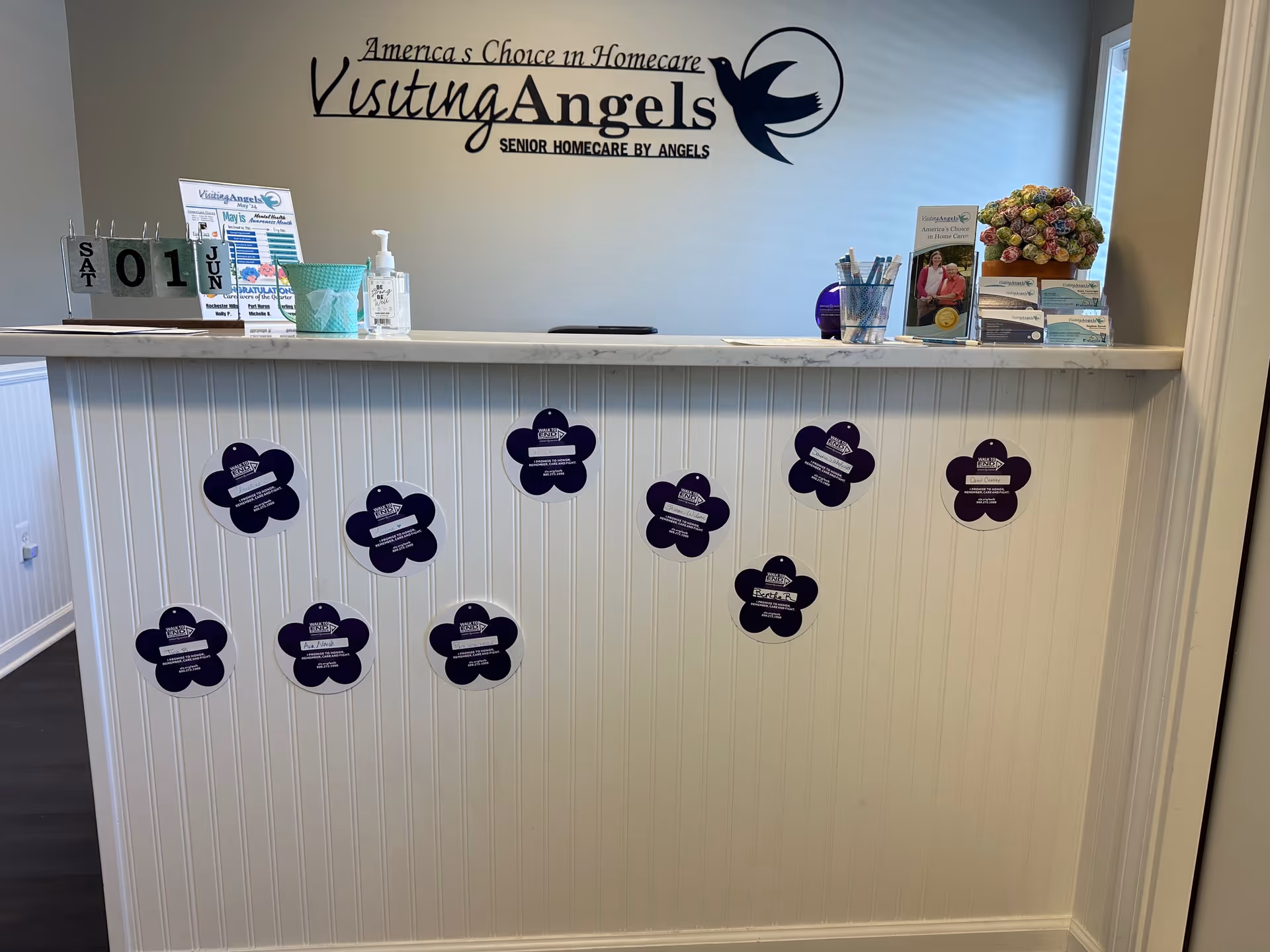 Reception desk inside Visiting Angels Senior Home Care with logo, brochures, and purple flower decals.