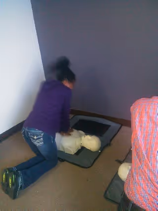 Caregiver performs CPR on a dummy mannequin in a small training room.