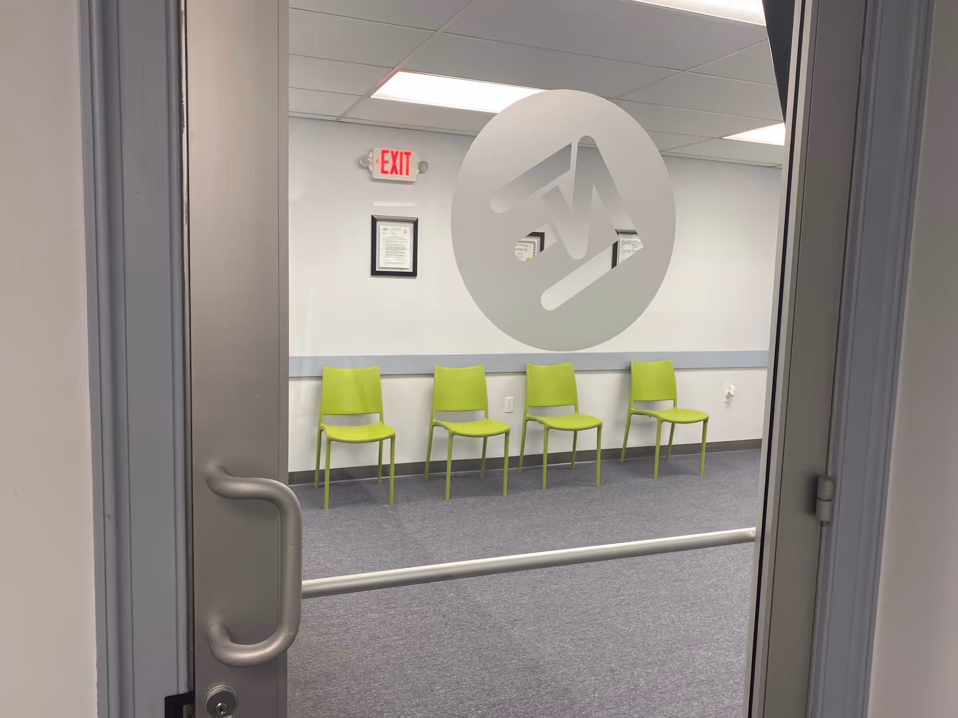 Interior hallway with lime green chairs along a wall and a frosted circular logo on glass