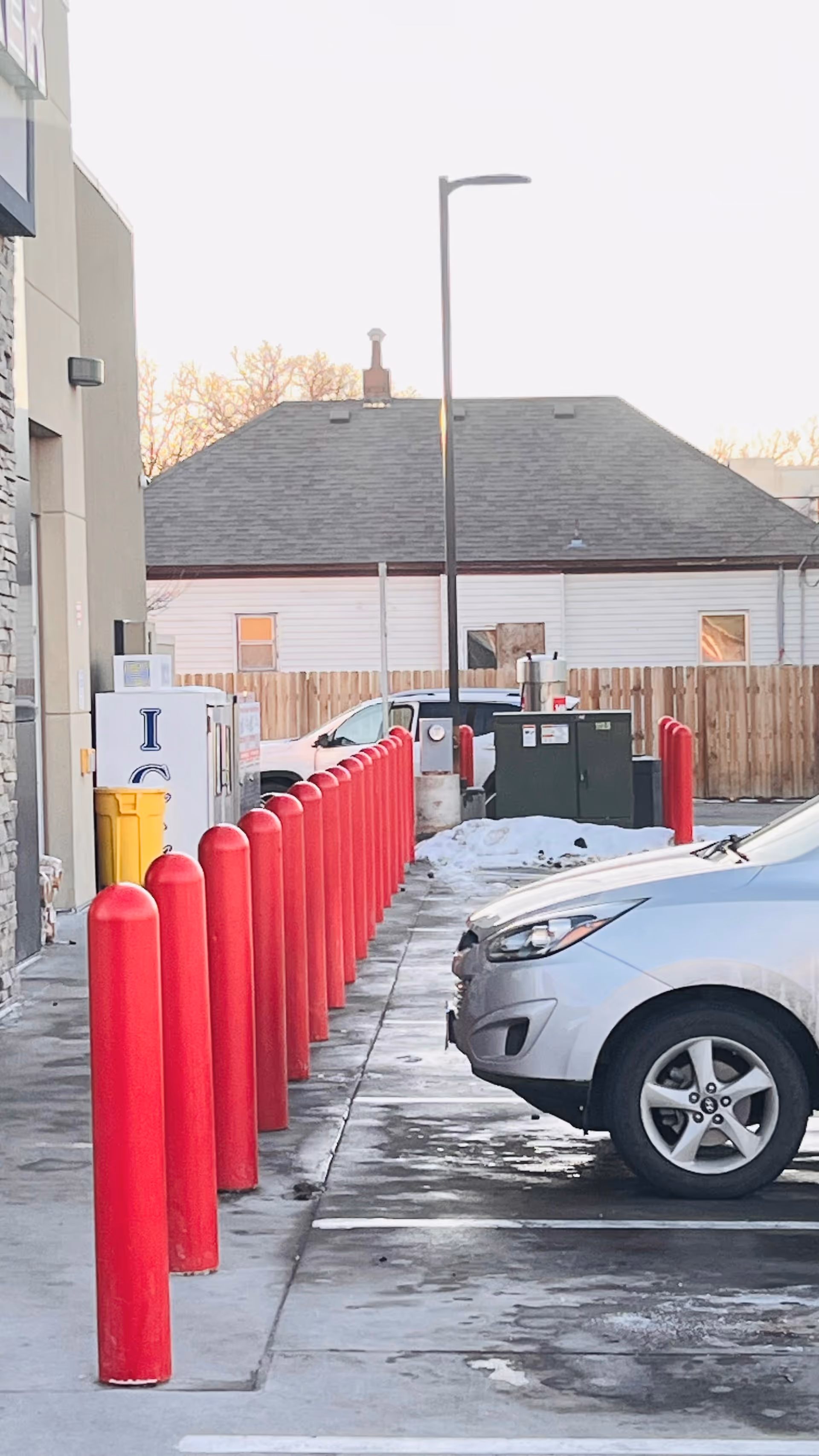 Exterior view of a facility's parking lot with red bollards, a white car, and a fence.