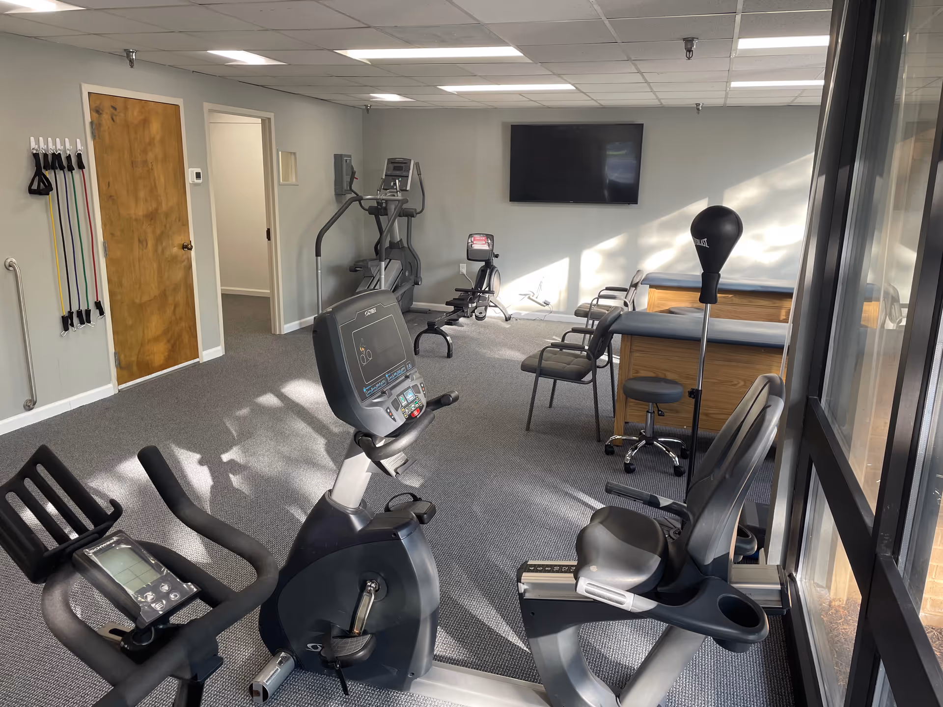 Indoor senior fitness gym with stationary bikes, treadmill, resistance bands, and seating.