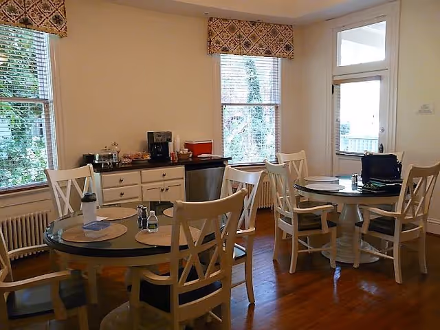 Bright dining room with round tables, white chairs, and a coffee station near windows.
