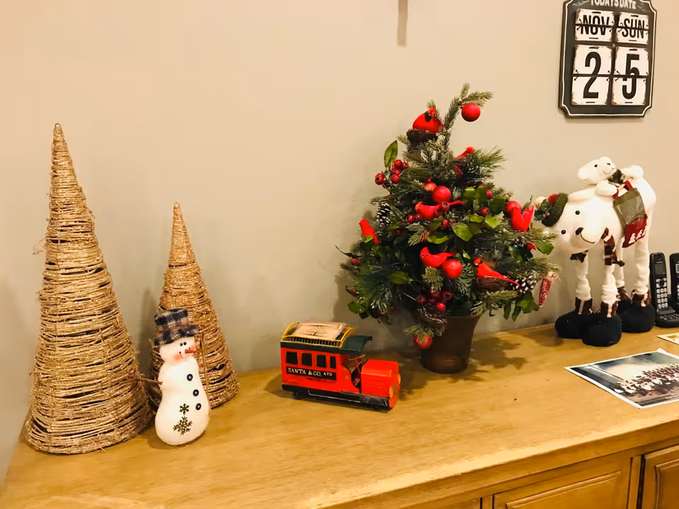 Holiday decorations on a wooden surface: woven cone trees, a snowman, a Christmas tree, and toys.