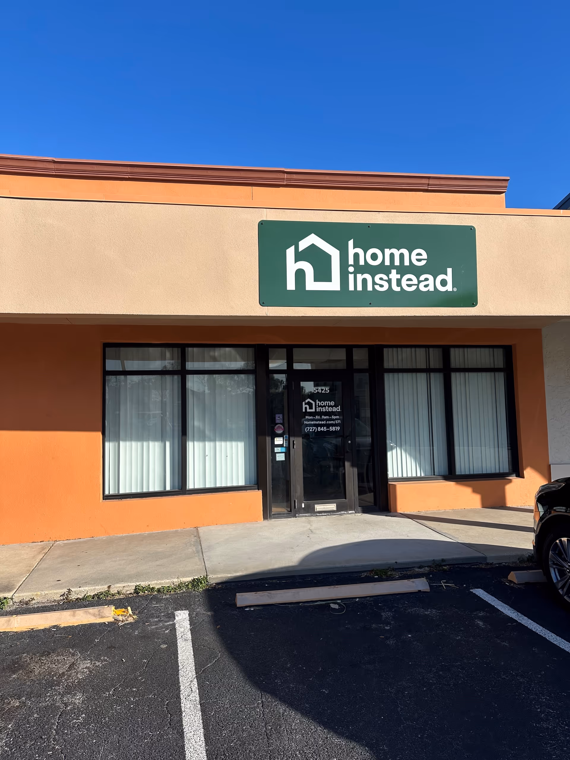 Orange storefront with a green Home Instead sign and glass entrance in bright daylight.