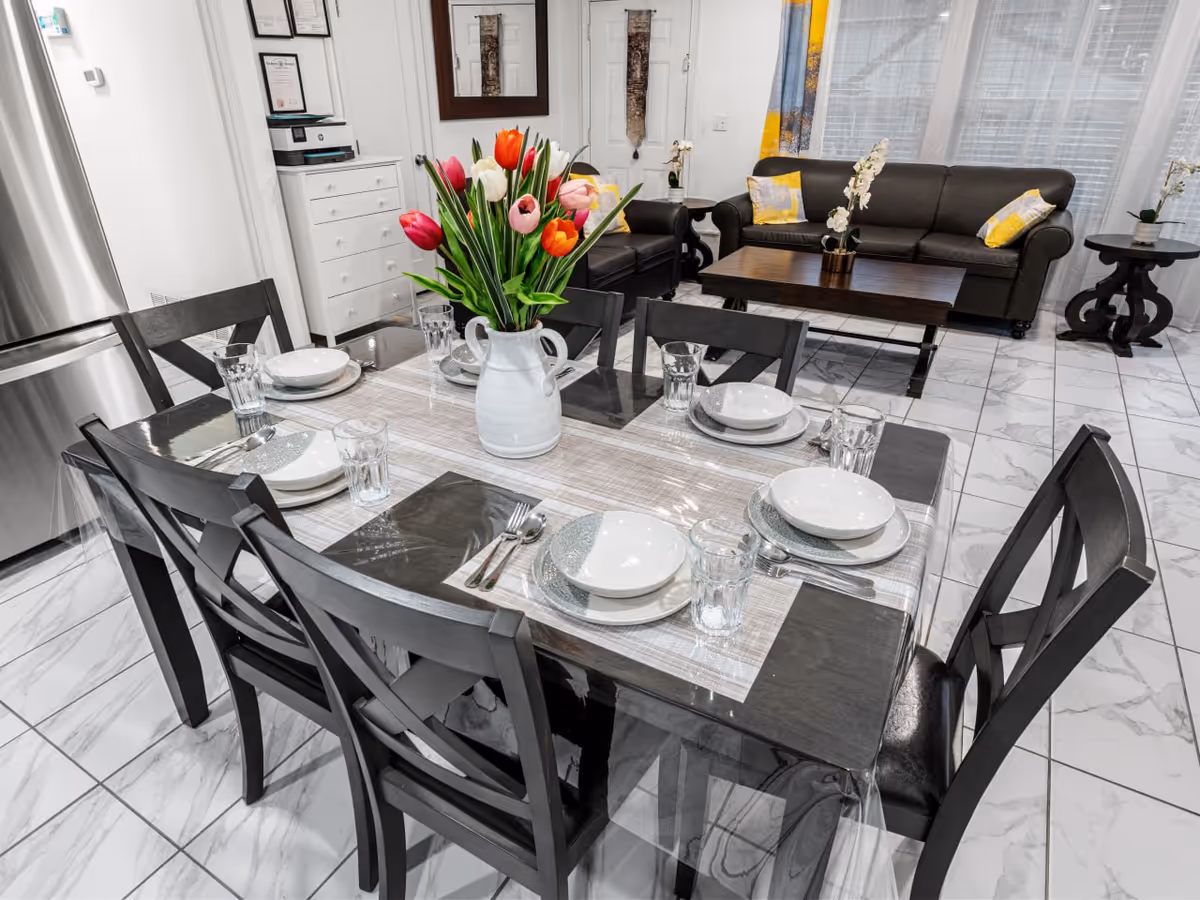 Modern dining area with a six-seat table set, vase of tulips, and living room beyond.