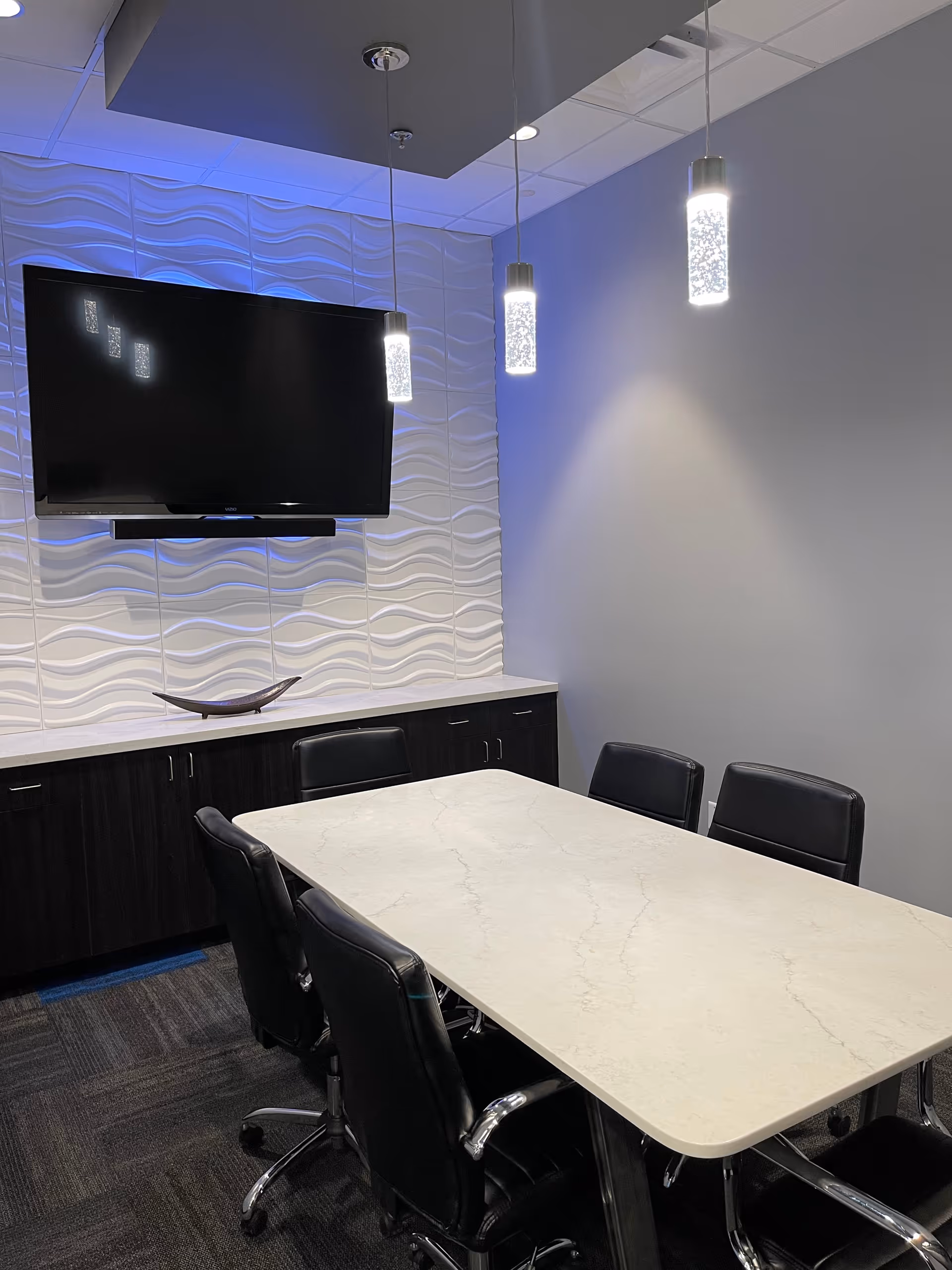 Modern conference room with marble table, black chairs, TV, and wave-pattern wall panels.