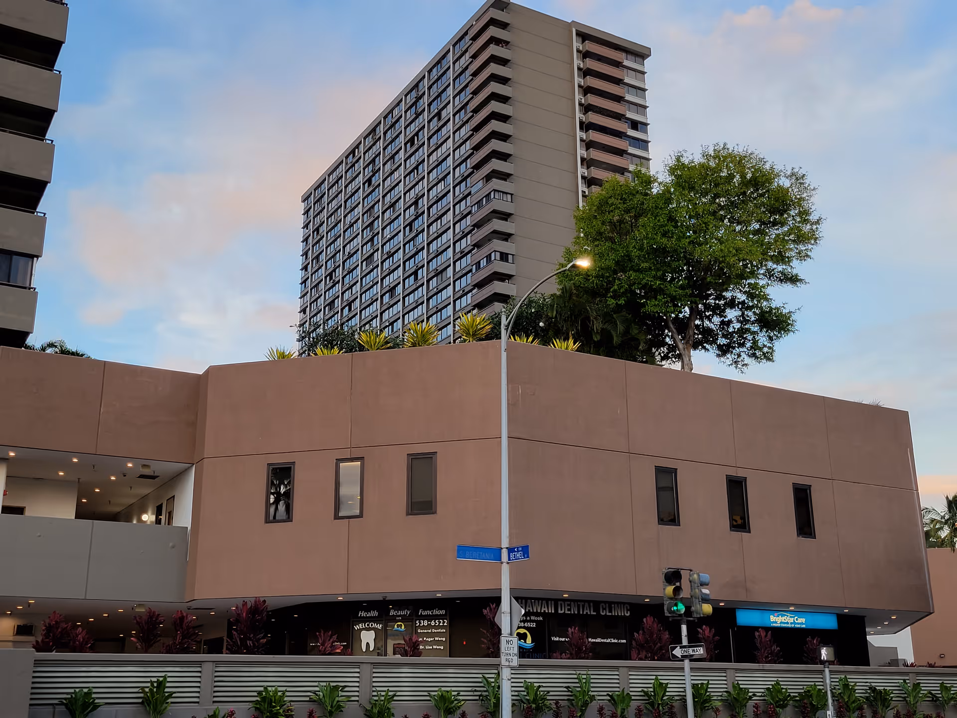 Tall brown building with a street sign, trees, and a dental clinic storefront.