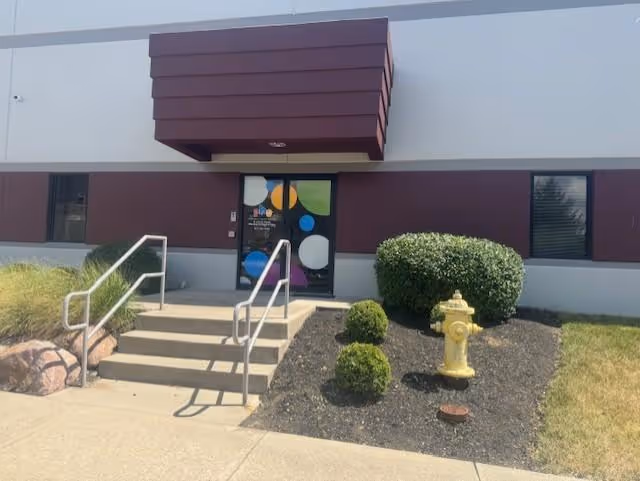 Exterior view of a building entrance with stairs, handrails, and landscaping.