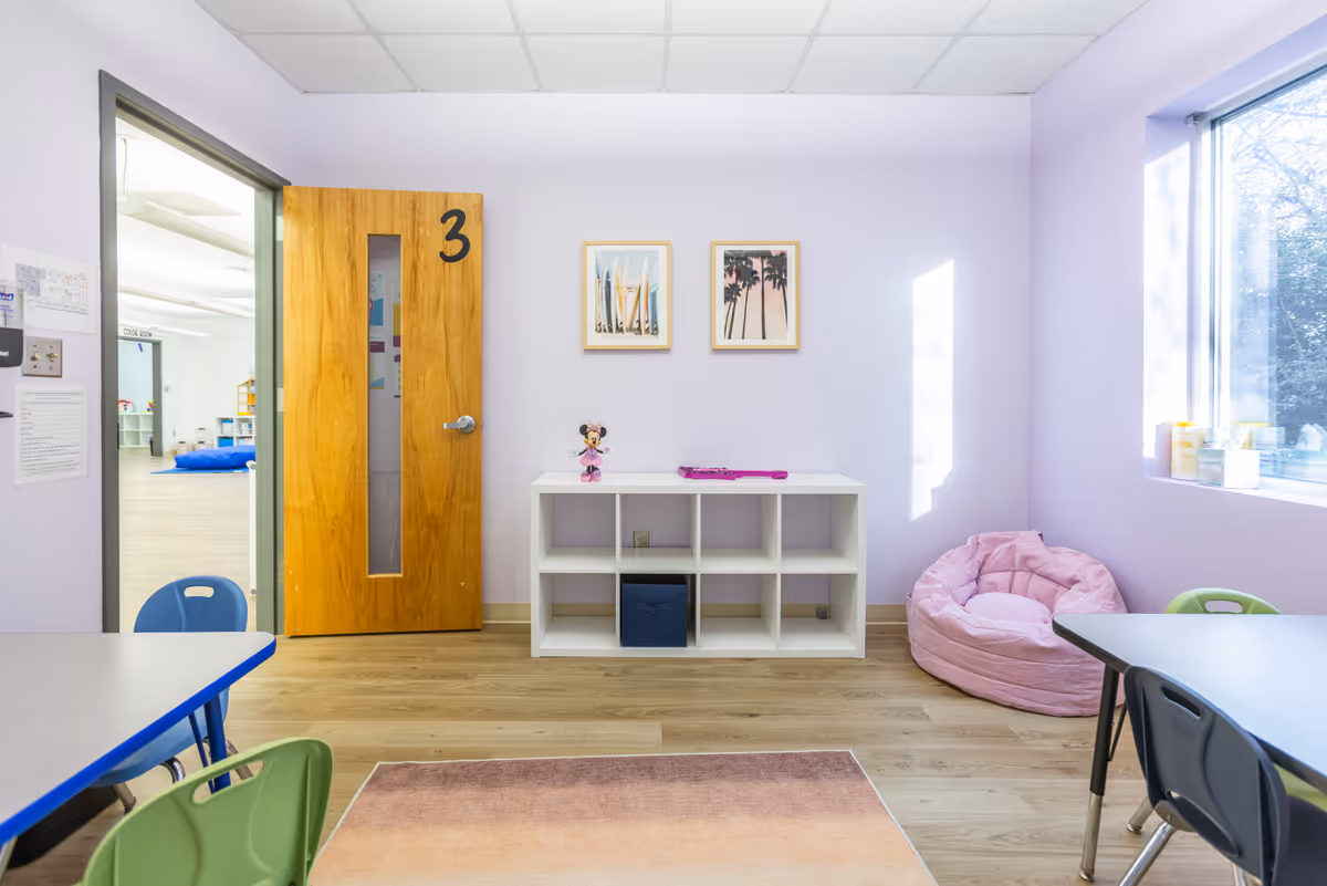 Pastel playroom in a senior facility with cubby shelving, bean bag chair, and small tables.