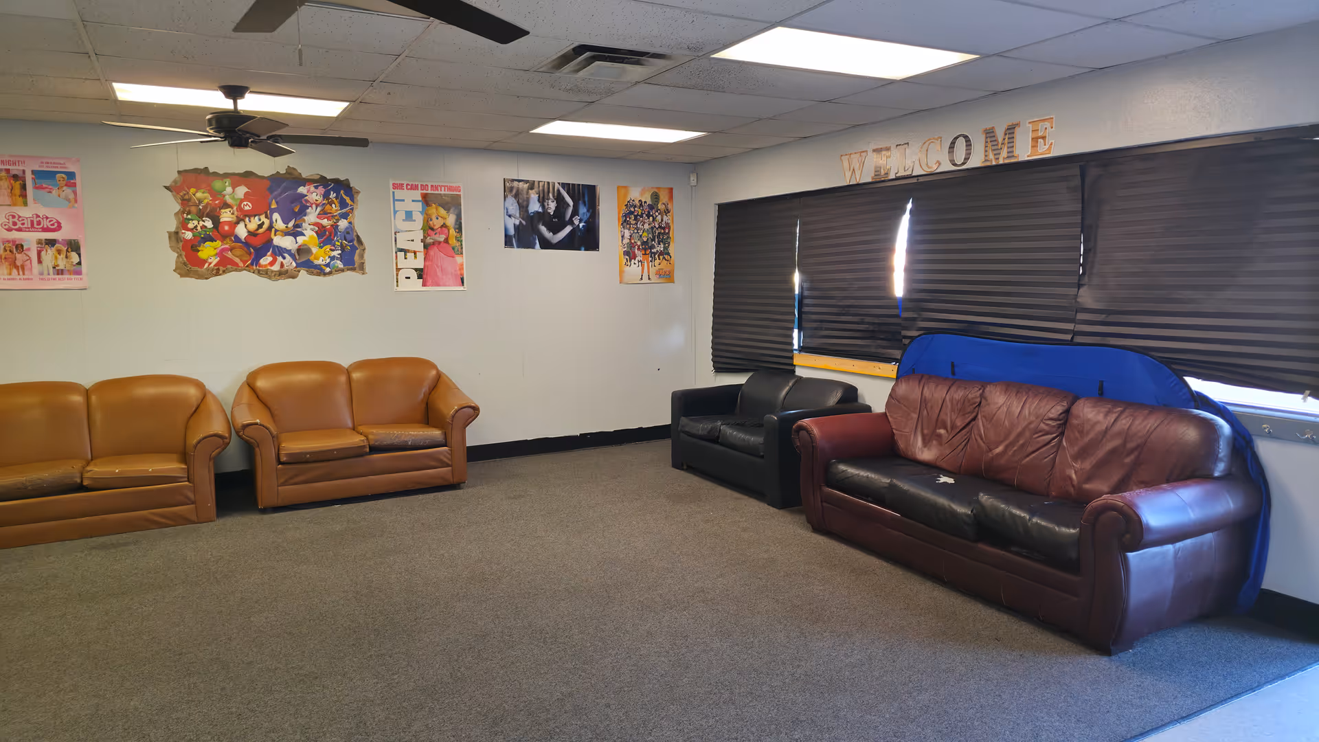 Interior lounge with several leather sofas, wall posters, and a 'WELCOME' sign.