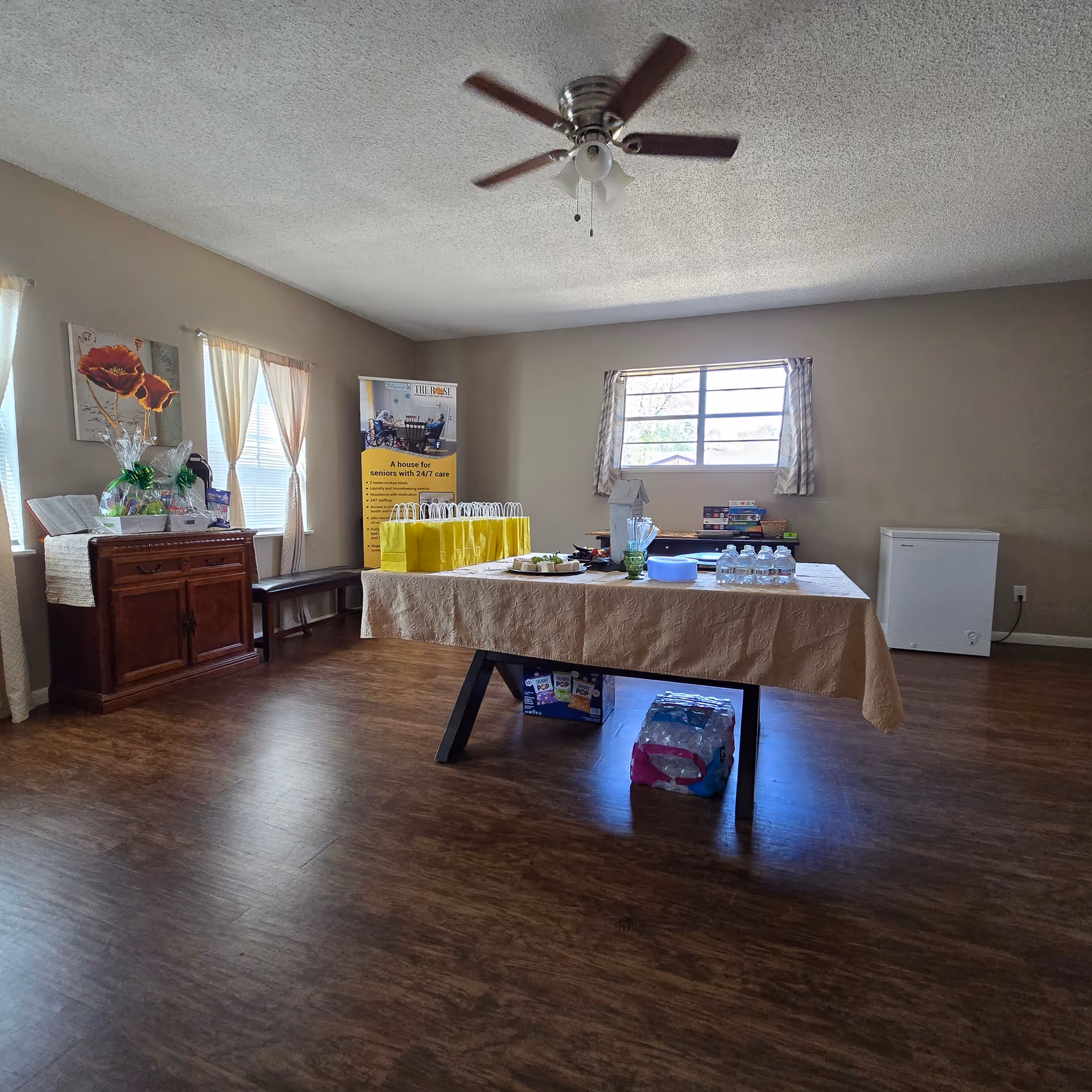 Interior room with a long beige-clothed table, yellow gift bags, water bottles, and banners.