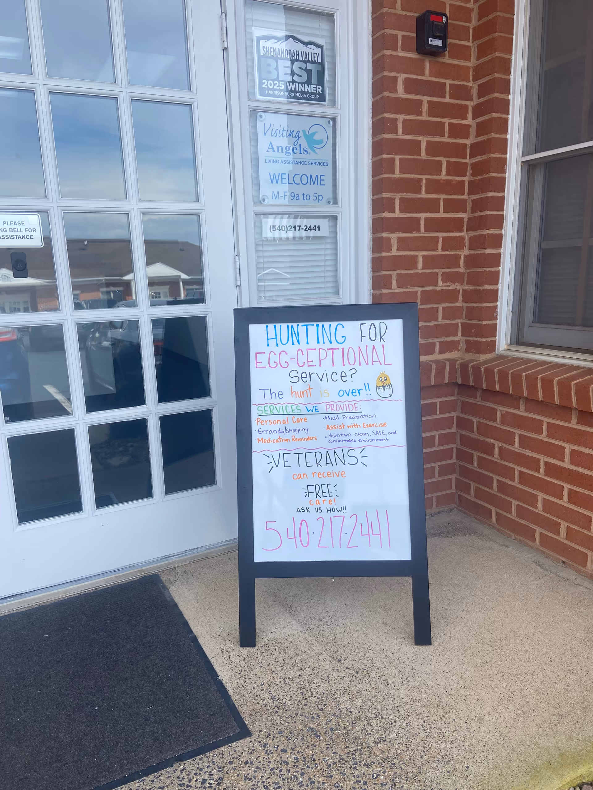 Exterior view of a brick building entrance with glass door and a chalkboard sign.
