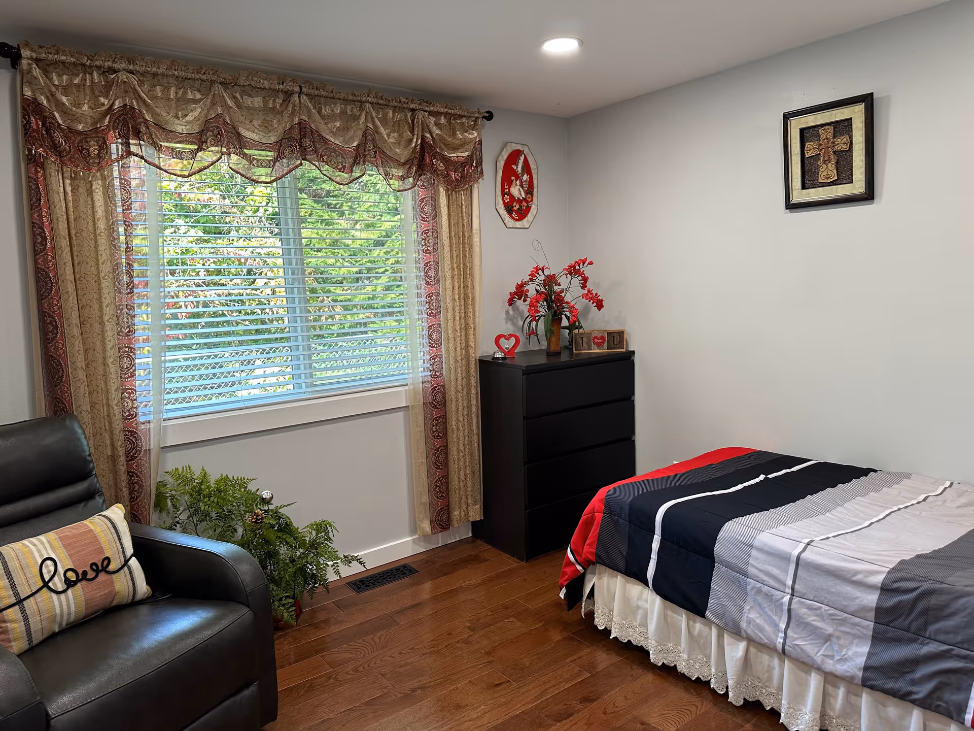 A cozy bedroom with a bed, dresser, window with curtains, and a chair.