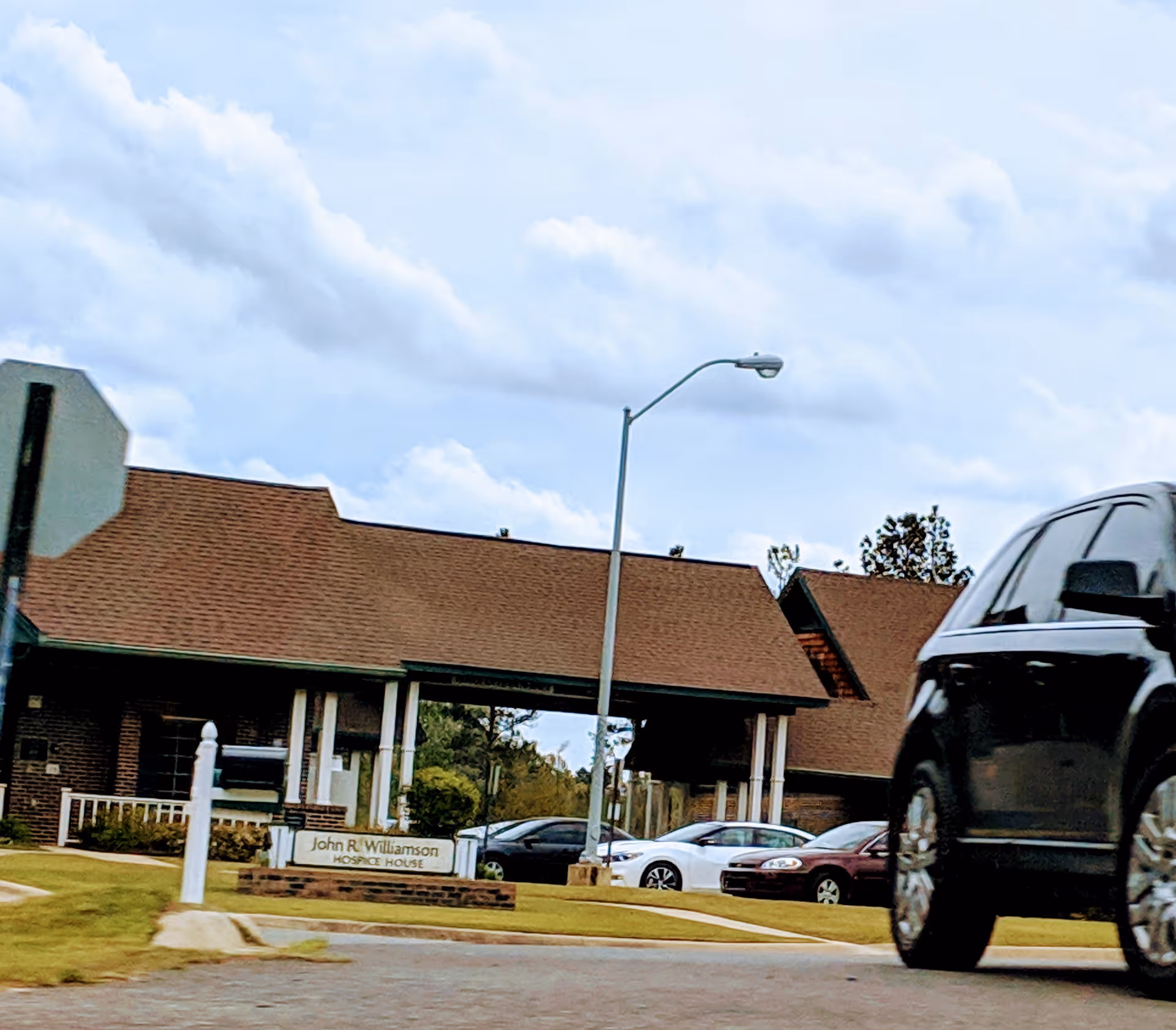Exterior view of a hospice building with a visible sign and parked cars.