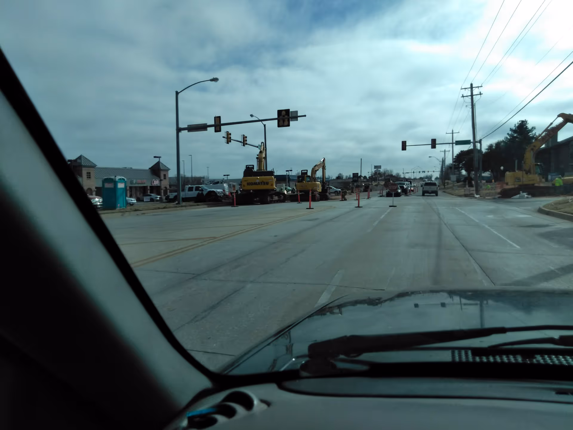 From inside a car, construction site with excavators and traffic signals on a wide street.